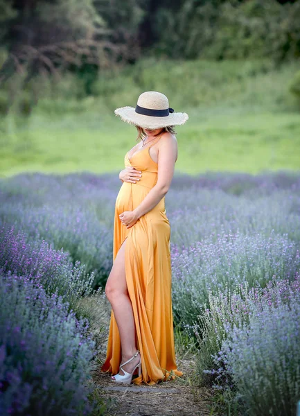 Gravid flicka i en hatt och en gul klänning promenader i en lavendel — Stockfoto