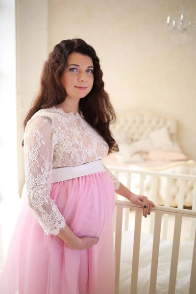 Fille enceinte dans un beau debout près de la crèche blanche — Photo