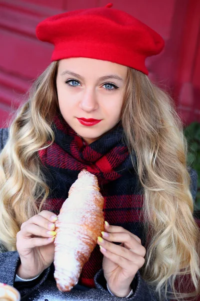 Mädchen mit roter Baskenmütze und grauem Mantel mit langen Locken und Croissant — Stockfoto