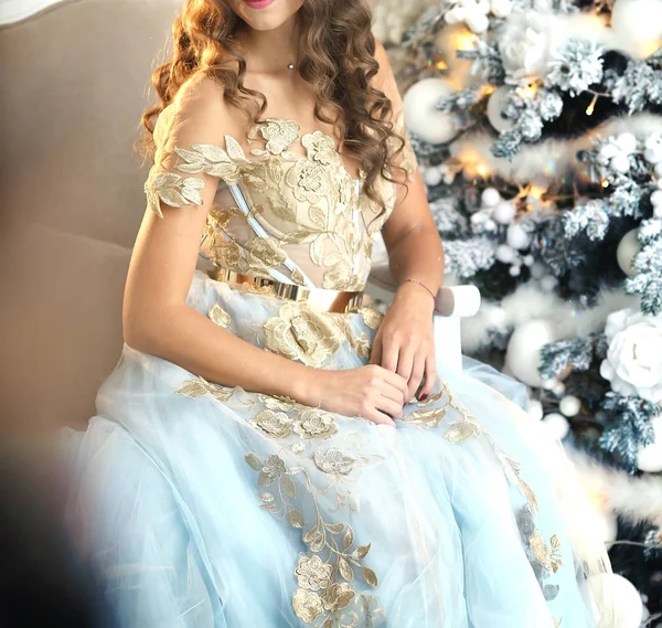 Luxuriöse Mädchen in einem schönen Kleid sitzt neben einem Weihnachtsbaum — Stockfoto