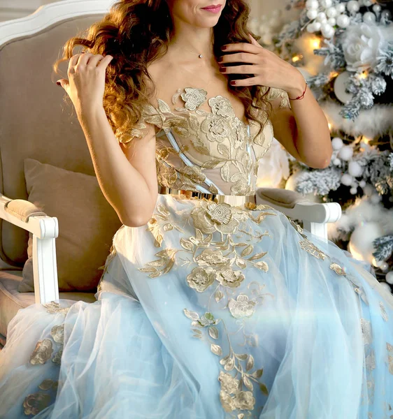 Luxuriöse Mädchen in einem schönen Kleid sitzt neben einem Weihnachtsbaum — Stockfoto