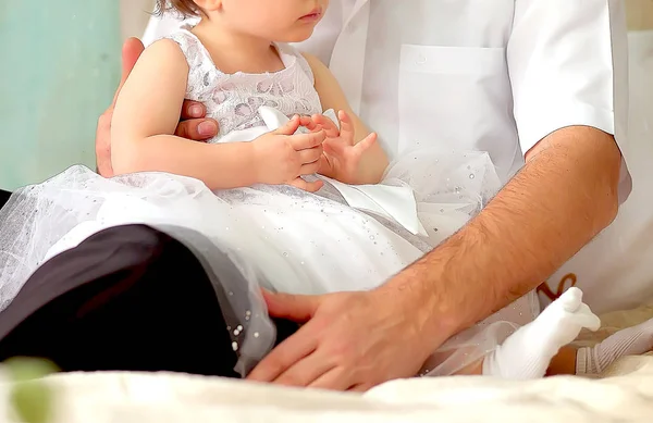 Μικρό κορίτσι κάθεται με τον μπαμπά στην αγκαλιά της σε ένα όμορφο λευκό φόρεμα — Φωτογραφία Αρχείου