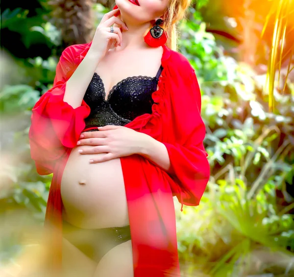 Terhes szőke lány piros tunikában és fülbevalóval a trópusi — Stock Fotó