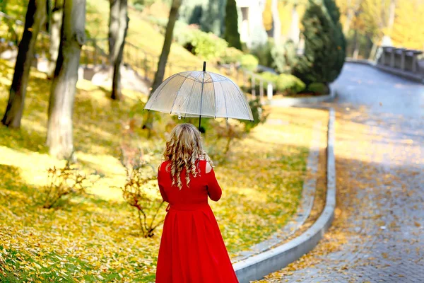 Belle femme en robe rouge se promène avec un parapluie dans le parc d'automne — Photo