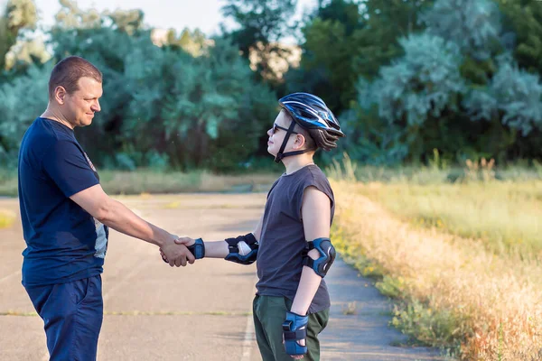 Father and son teenager in helmet and black T-shirt spend time together on the playground shake hands. Strong male handshake. Father and son. Family holiday. Health and Sports Concept