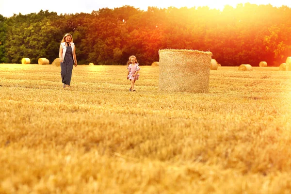 Mom and daughter Caucasians walk with a smile on a mown wheat field where there are huge sheaves. Family fun and fun. Nature. Harvesting. Agriculture. Cereals. Rural life. Rest in the countryside.
