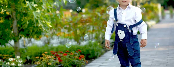 Kot pantolon ve beyaz gömlekli küçük bir çocuk bahçede sabun köpüğüyle oynuyor. Neşe. Çocukluk. Duygular. Uzayı sola kopyala