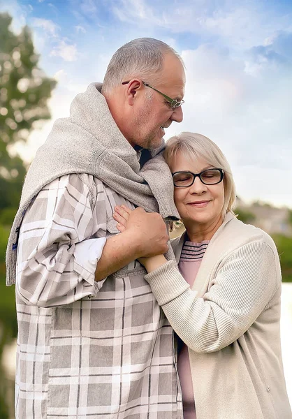 Old age, relationships and people concept - happy senior couple hugging in nature. The husband hugs his wife tenderly. Caring, love