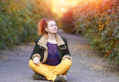 Genç bir kadının portresi gözlerini kapadı ve sonbahar parkında asfalt bir yolda otururken nilüfer pozisyonunda rahatladı. Sakin ve meditasyon konsepti. Boşluğu kopyala