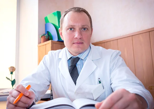 Νεαρός Καυκάσιος Γιατρός Ένα Χαμόγελο Ένα Λευκό Παλτό Κάθεται Στο — Φωτογραφία Αρχείου