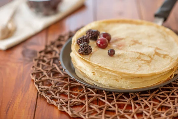 A stack of homemade pancakes on a frying pan, brown background with berries