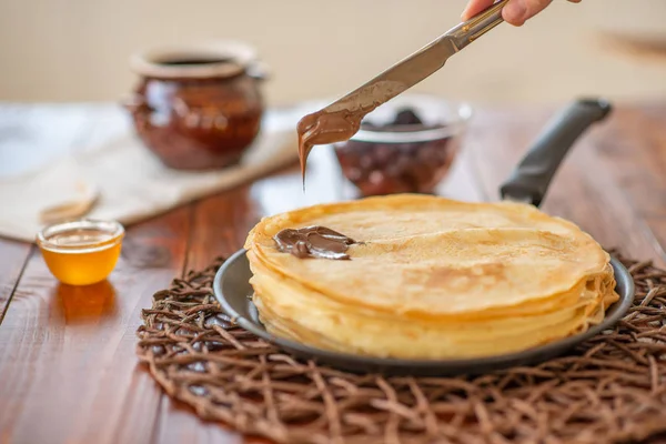 A stack of homemade pancakes on a frying pan with chocolate on brown background