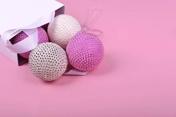 Ροζ Χριστουγεννιάτικα μπαλάκια από ένα λευκό πακέτο σε ένα ροζ φόντο — Φωτογραφία Αρχείου