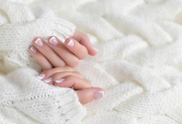 Mãos bonitas das mulheres com manicure francês no fundo de uma camisola quente branca — Fotografia de Stock