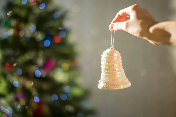 Vrouwelijke hand versieren kerstboom door bel op heldere achtergrond met bokeh — Stockfoto