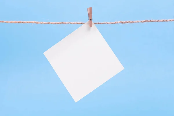 Ένα λευκό τετράγωνο χαρτί σημείωμα κρέμεται σε μανταλάκια σε μπλε φόντο, mock up — Φωτογραφία Αρχείου
