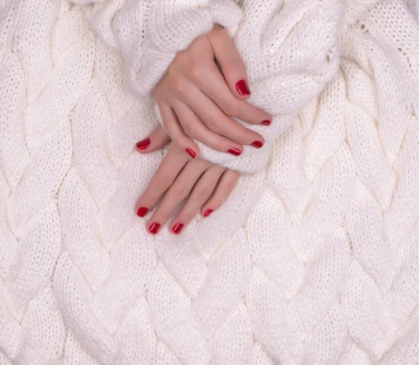Women's beautiful hands with red manicure on the background of a white warm sweater, top view — Stockfoto