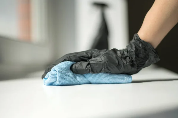 En hand i svarta handskar håller en microfiber rengöringsduk och en spray med sterilisering gör desinfektion för god hygien — Stockfoto