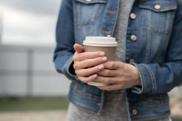 Womens hands in a denim jacket hold a Cup of coffee to go, zero west