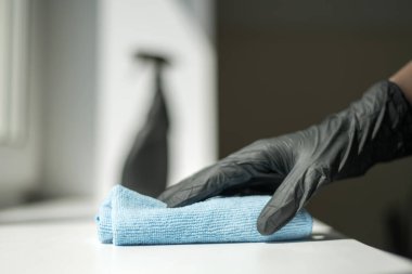 Siyah eldivenli bir el mikrofiber temizleme bezi ve sterilize edilmiş bir sprey iyi bir hijyen için dezenfekte yapar.