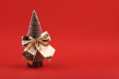 Kırmızı arka planda izole edilmiş bir yay ile süslenmiş Noel ağacı