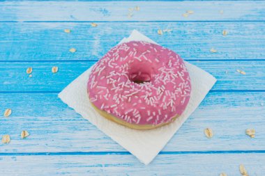 Lezzetli tatlı pembe çörek üzerinde kağıt üzerine çizilmiş mavi beyaz yüksek kontrast bütün tahıl yulaf yemek üstünde o ile ahşap arka plan portre