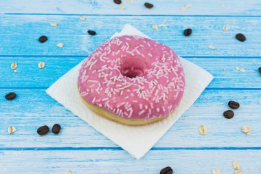 Lezzetli tatlı pembe çörek üzerinde kağıt üzerine çizilmiş mavi beyaz yüksek kontrast tahıl yulaf yemek ve kahve çekirdekleri ile ahşap arka plan üzerinde portre