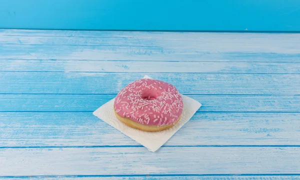 Lezzetli tatlı pembe çörek üzerinde kağıt üzerine çizilmiş mavi beyaz yüksek karşıtlık ahşap arka plan en iyi açı