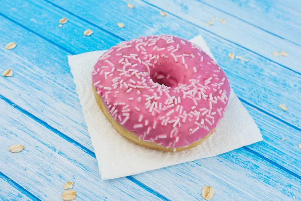 Lezzetli tatlı pembe çörek üzerinde kağıt üzerine çizilmiş mavi beyaz yüksek kontrast bütün tahıl yulaf yemek üstünde o ile ahşap arka plan portre