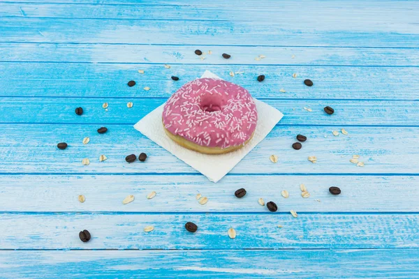 Lezzetli tatlı pembe çörek üzerinde kağıt üzerine çizilmiş mavi beyaz yüksek kontrast tahıl yulaf yemek ve kahve çekirdekleri ile ahşap arka plan üzerinde portre