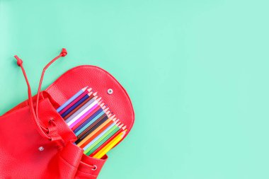 Mavi arka planda okul ekipmanları için kırmızı çanta. İçinde renkli kalemler olan okul çantası..