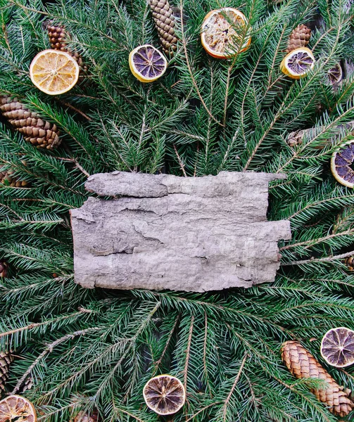 Navidad, Año Nuevo vacaciones de invierno composición de estilo vintage. Trozo de corteza de árbol en ramas de abeto verde decorado con rodajas de naranja seca y conos . — Foto de Stock