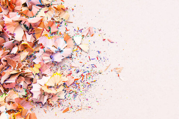 Wooden pencil shavings and colorful crumbs of graphite from sharpener on soft pink paper background. Top view. Design elements for poster, banner, cards.