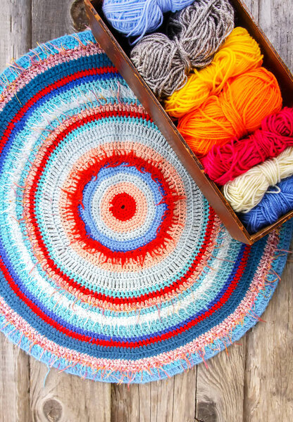 Knitted striped mat and colorful skeins of wollen yarn on wooden background.