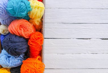 Beyaz tahta arka planda ahşap kutuda renkli iplik topları.