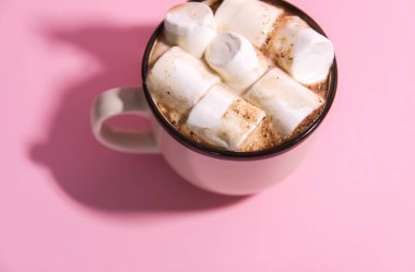 Küçük çocuğun elleri seramik bardakla sıcak sıcak kakao bardağı ve yumuşak pembe arka planda lokum tutuyor..