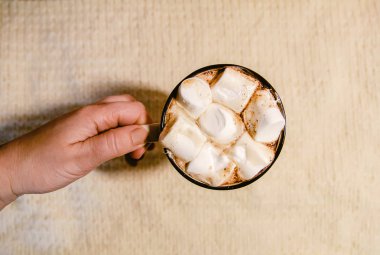 Woman's hand holding ceramic mug with hot fresh cocoa drink with marshmallows