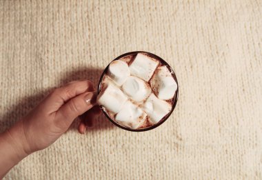 Woman's hand holding ceramic mug with hot fresh cocoa drink with marshmallows