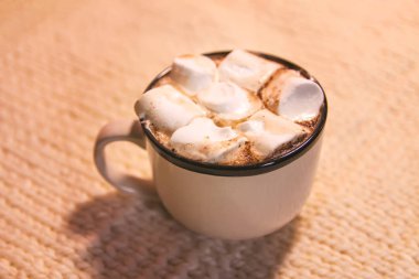 Hot fresh cocoa drink in a ceramic mug with melting sweet marshmallows on cozy knitted background