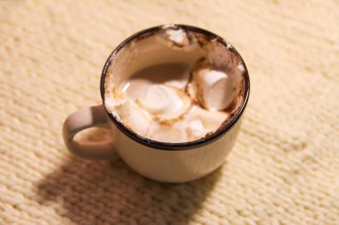 Hot fresh cocoa drink in a ceramic mug with melting sweet marshmallows on cozy knitted background