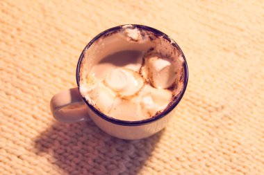 Hot fresh cocoa drink in a ceramic mug with melting sweet marshmallows on cozy knitted background