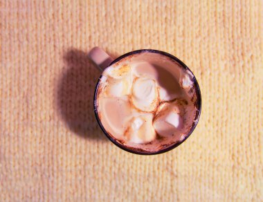 Hot fresh cocoa drink in a ceramic mug with melting sweet marshmallows on cozy knitted background