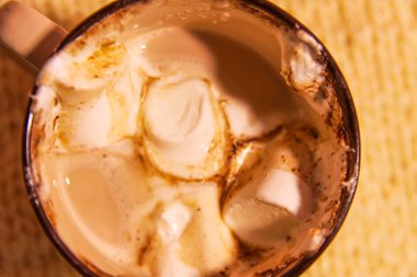 Hot fresh cocoa drink in a ceramic mug with melting sweet marshmallows on cozy knitted background