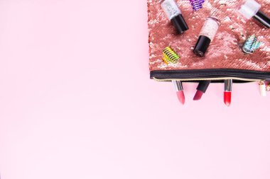 Bright composition of fashion accessories. Glitter sequins cosmetic bag with nail polishes, lipsticks, hair pins. Objects on soft pastel background. Flat lay, top view