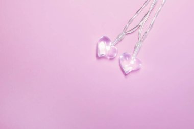 Yumuşak pembe arka planda iki küçük cam şeffaf kalp. Sevgililer Günü sembolü. Dekoratif unsur. Sevgililer Günü Kartı.