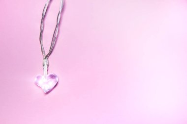Yumuşak pembe arka planda küçük şeffaf cam kalp. Sevgililer Günü sembolü. Dekoratif unsur. Sevgililer Günü Kartı.