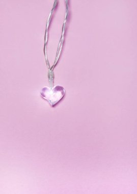 Yumuşak pembe arka planda küçük cam şeffaf kalp. Sevgililer Günü sembolü. Dekoratif unsur. Sevgililer Günü Kartı.