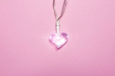 Yumuşak pembe arka planda küçük şeffaf cam kalp. Sevgililer Günü sembolü. Dekoratif unsur. Sevgililer Günü Kartı.