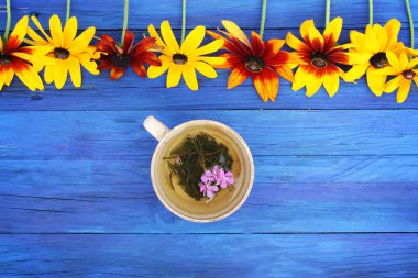 Natural herbal tea with purple fresh flowers and leaves of medical fireweed plant n ceramic cup on blue wooden boards outdoors. clipart