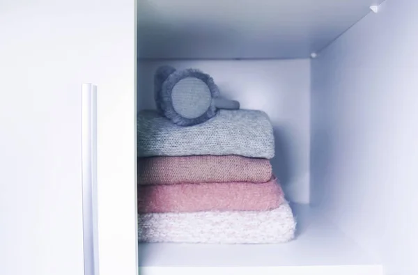 White shelf of the home wardrobe with colorful sweaters, jumpers and warm headphones. Small space organization. Minimalism concept.